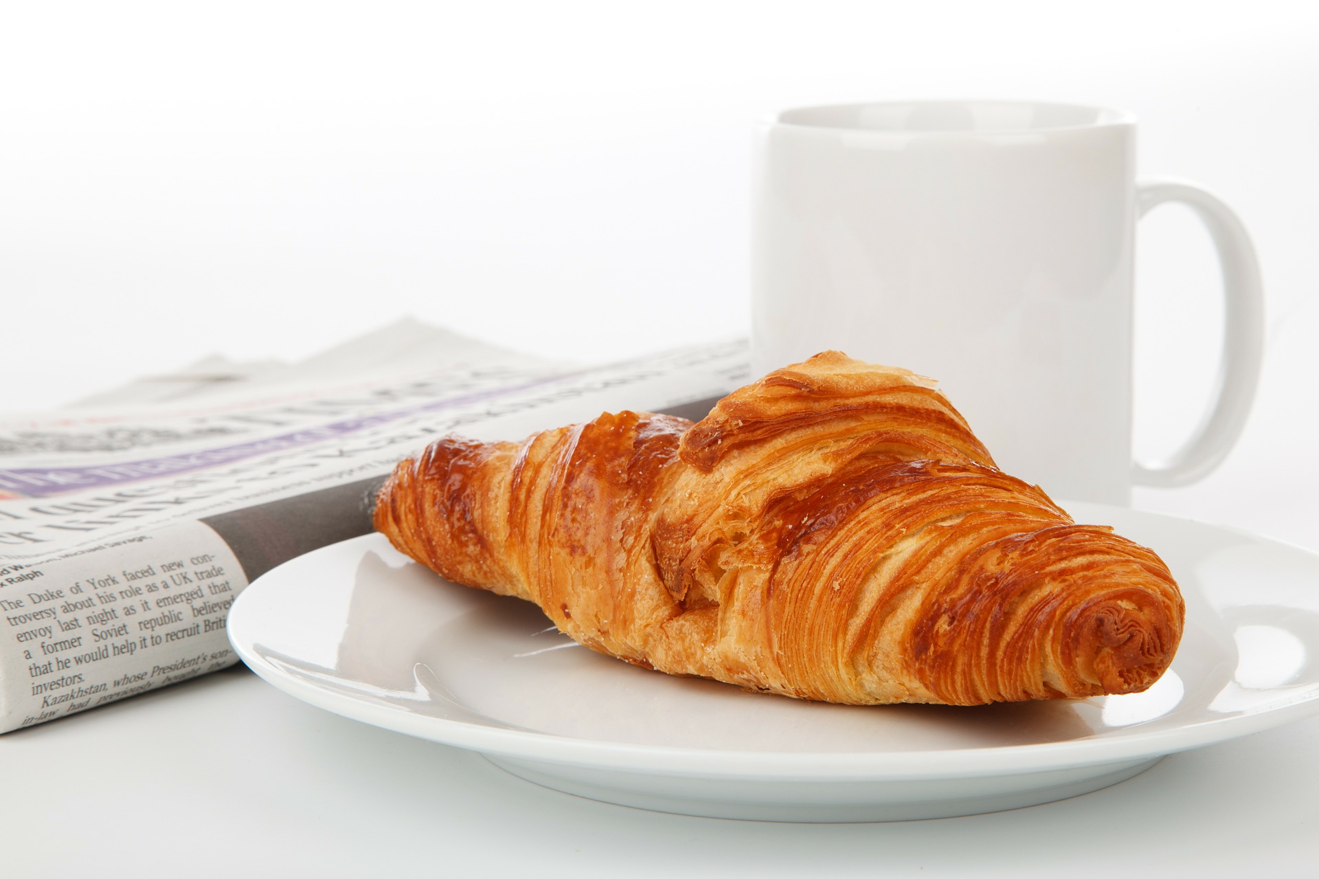 Zeitung, Tasse und Croissant